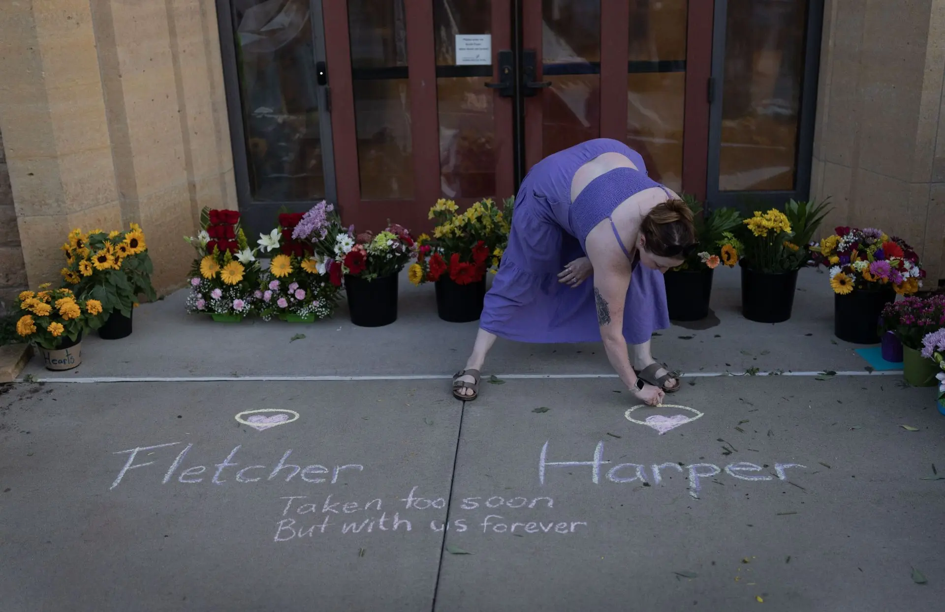 Grace Mfinanga, an Annunciation School graduate, chalks a message at a memorial for victims of yesterday's shooting in front of Annunciation Catholic Church on August 28, 2025 in Minneapolis, Minnesota (Image via Getty)