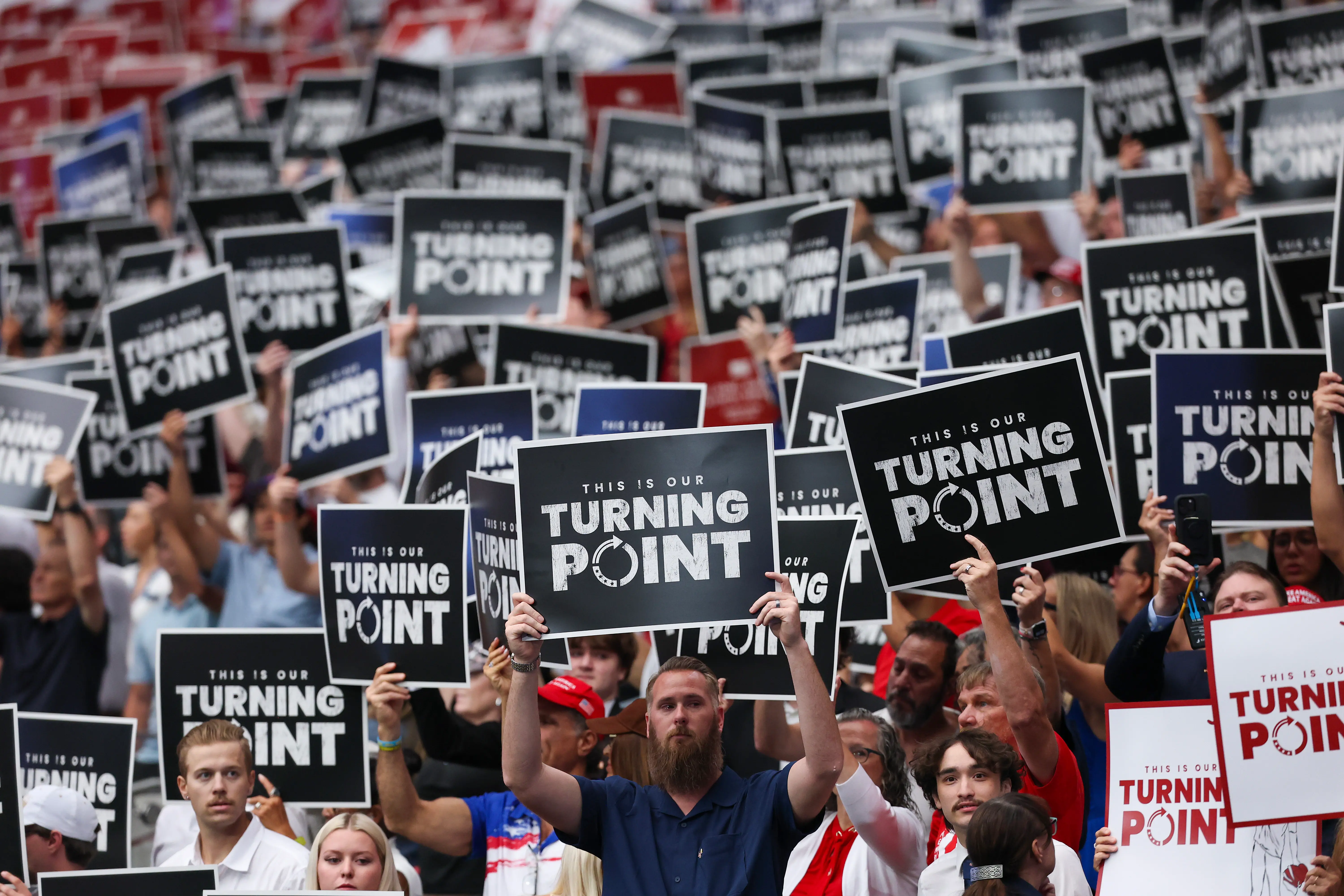 GLENDALE, ARIZONA - SEPTEMBER 21: Attendees hold up Turning Point USA signs at the memorial service for political activist Charlie Kirk at State Farm Stadium on September 21, 2025 in Glendale, Arizona. Kirk, the CEO and co-founder of Turning Point USA, was shot and killed on September 10th while speaking at an event during his "American Comeback Tour" at Utah Valley University. (Photo by Eric Thayer/Getty Images)