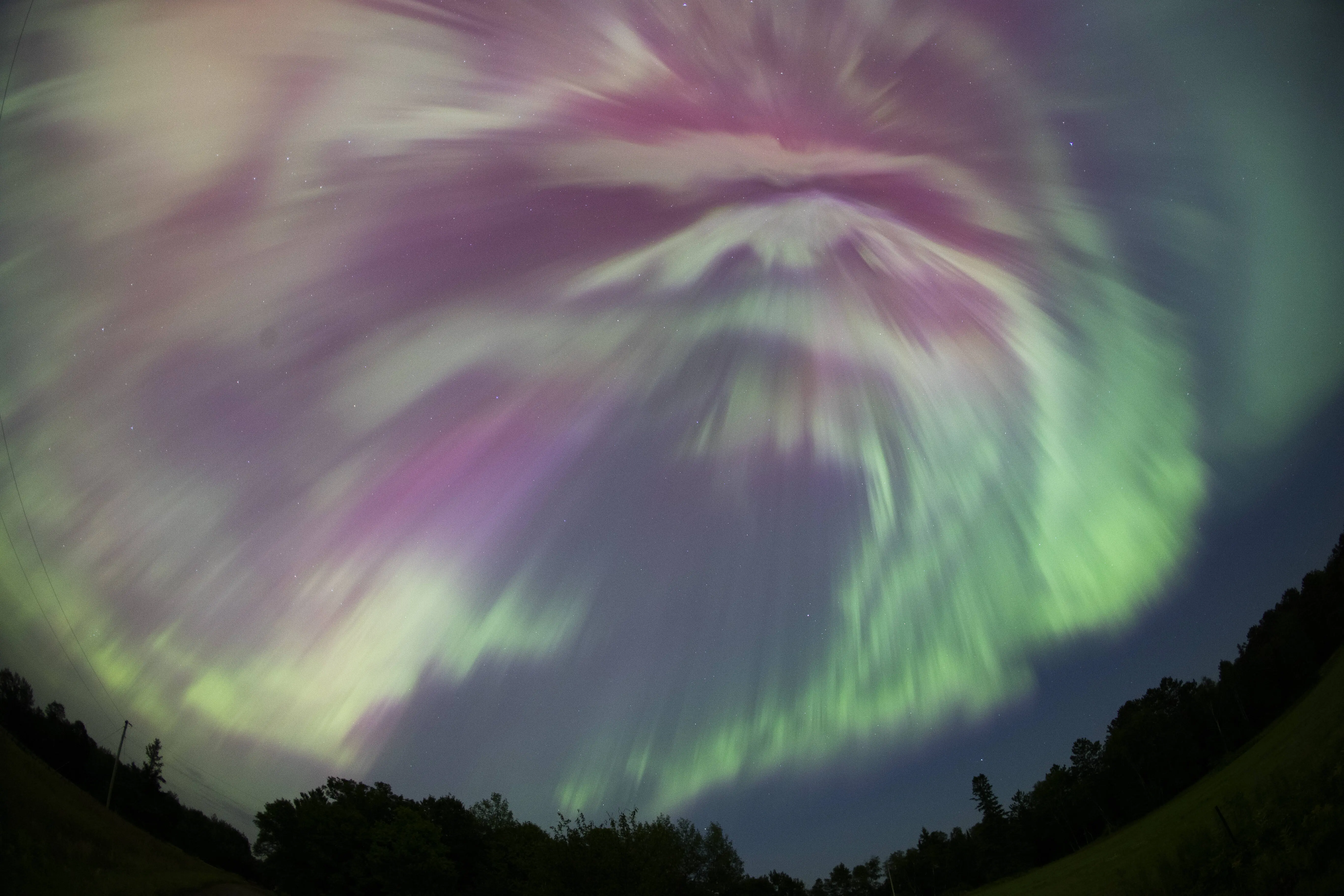 MINNESOTA, UNITED STATES - AUGUST 12: (EDITORS NOTE: This image was shot with a fisheye lens.) The northern lights (Aurora Borealis) illuminates the sky as a geomagnetic storm is bringing vibrant green and pink colors, during the peak of the Perseid meteor shower in Aitkin, Minnesota, United States on August 12, 2024. (Photo by Christopher Mark Juhn/Anadolu via Getty Images)