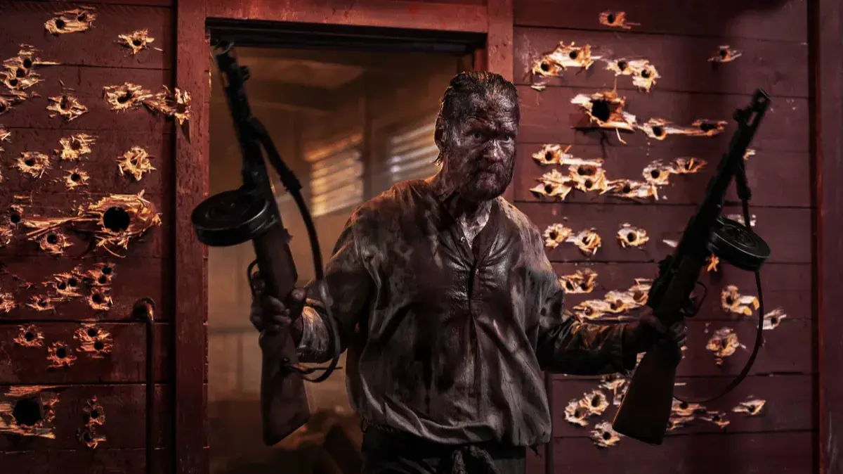 Aatami Korpi Jorma Tommila steps from a bullet riddled doorway carrying two PPSh 41 drum guns in Sisu: Road to Revenge. Image via Sony pictures.