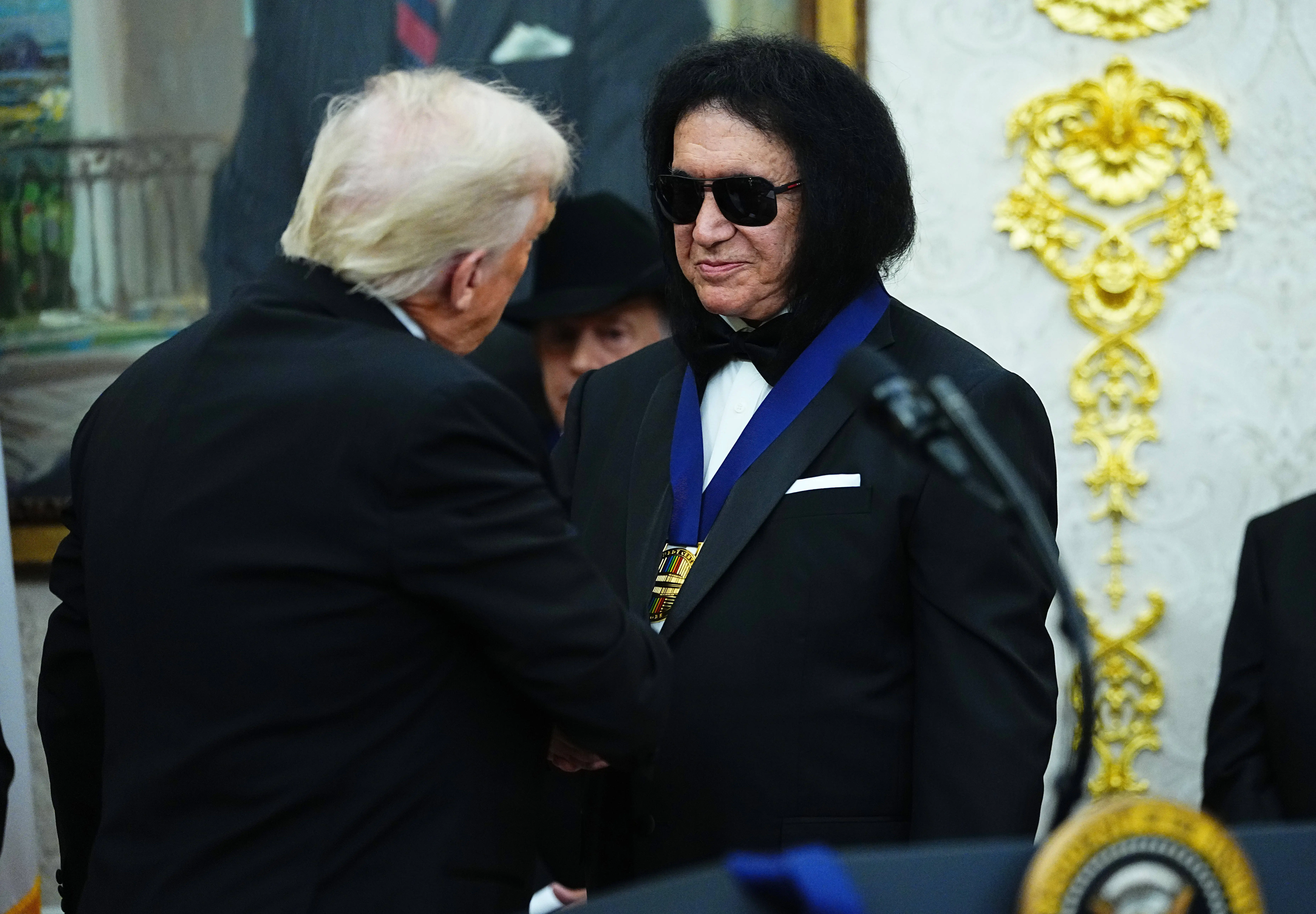 WASHINGTON, DC - DECEMBER 06: U.S. President Donald Trump (L) presents musician Gene Simmons (R) of the rock band KISS a medal for the 2025 Kennedy Center Honorees during a medal presentation in the Oval Office of the White House on December 06, 2025 in Washington, DC. The 2025 Kennedy Center honorees are Sylvester Stallone, George Strait, the rock band KISS, Gloria Gaynor, and Michael Crawford. (Photo by Aaron Schwartz/Getty Images)