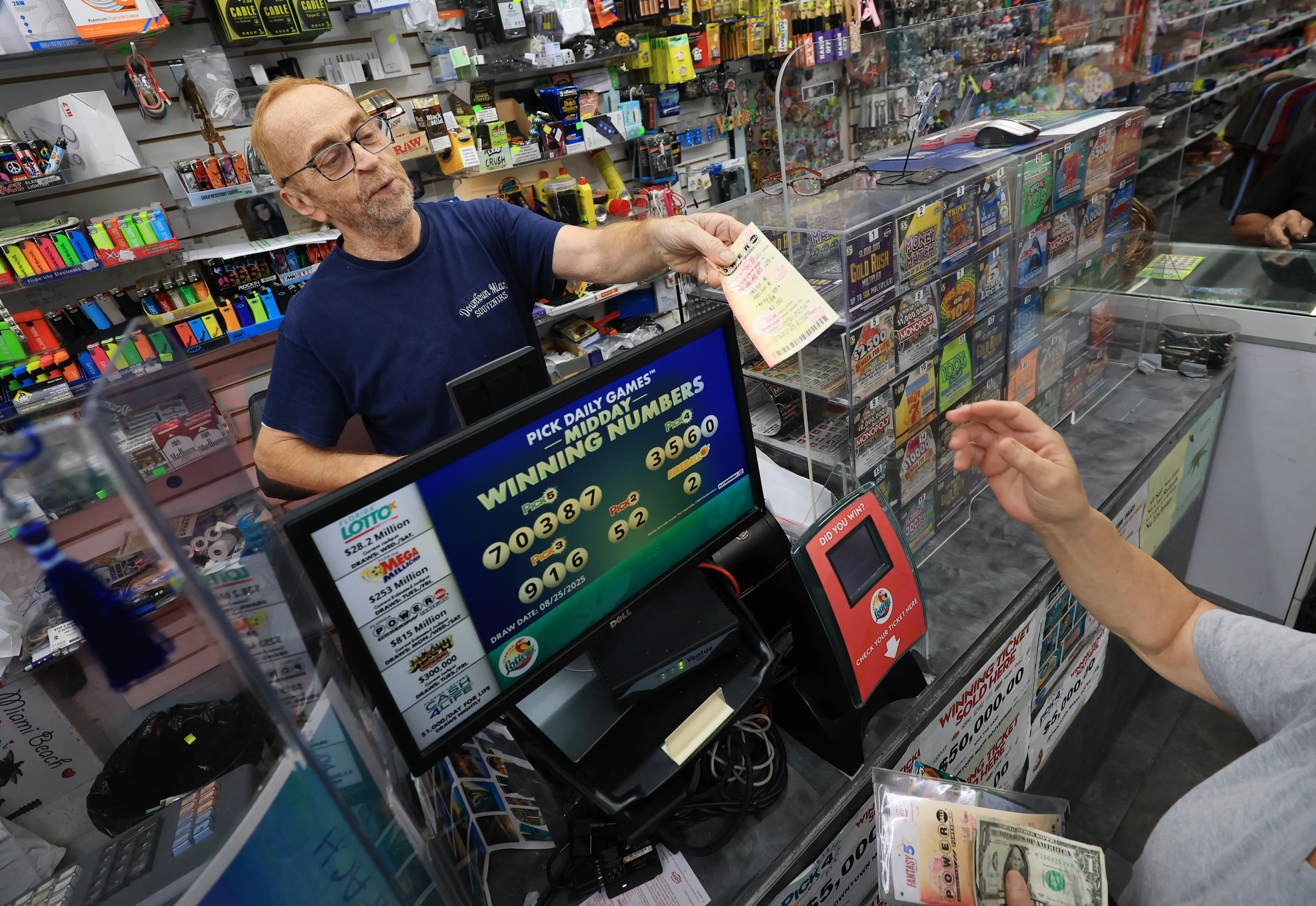 MIAMI, FLORIDA - AUGUST 26:  Robert Hadad sells Powerball lottery tickets to a customer at his Downtown Miami Souvenirs store on August 26, 2025 in Miami, Florida. The Powerball jackpot has climbed to $815 million ahead of Wednesday's drawing, making the jackpot the 10th-largest in Powerball history. (Photo by Joe Raedle/Getty Images)