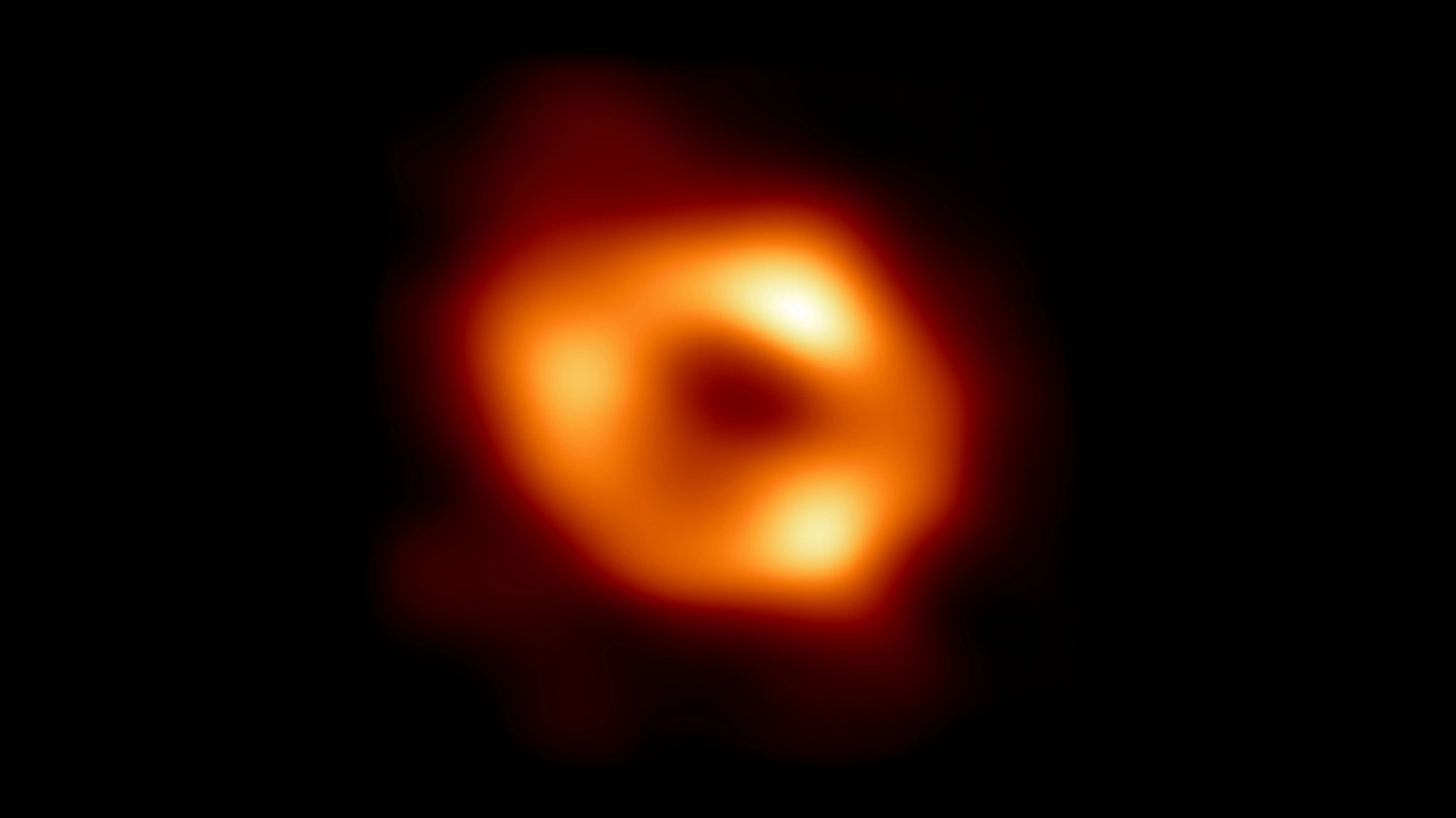 In this handout photo provided by NASA,  This is the first image of Sgr A*, the supermassive black hole at the centre of our galaxy, with an added black background to fit wider screens. It's the first direct visual evidence of the presence of this black hole. It was captured by the Event Horizon Telescope (EHT), an array which linked together eight existing radio observatories across the planet to form a single Earth-sized virtual telescope. The telescope is named after the event horizon, the boundary of the black hole beyond which no light can escape.   The image of the Sgr A* black hole is an average of the different images the EHT Collaboration has extracted from its 2017 observations.  In addition to other facilities, the EHT network of radio observatories that made this image possible includes the Atacama Large Millimeter/submillimeter Array (ALMA) and the Atacama Pathfinder EXperiment (APEX) in the Atacama Desert in Chile, co-owned and co-operated by ESO is a partner on behalf of its member states in Europe (Image via Getty)