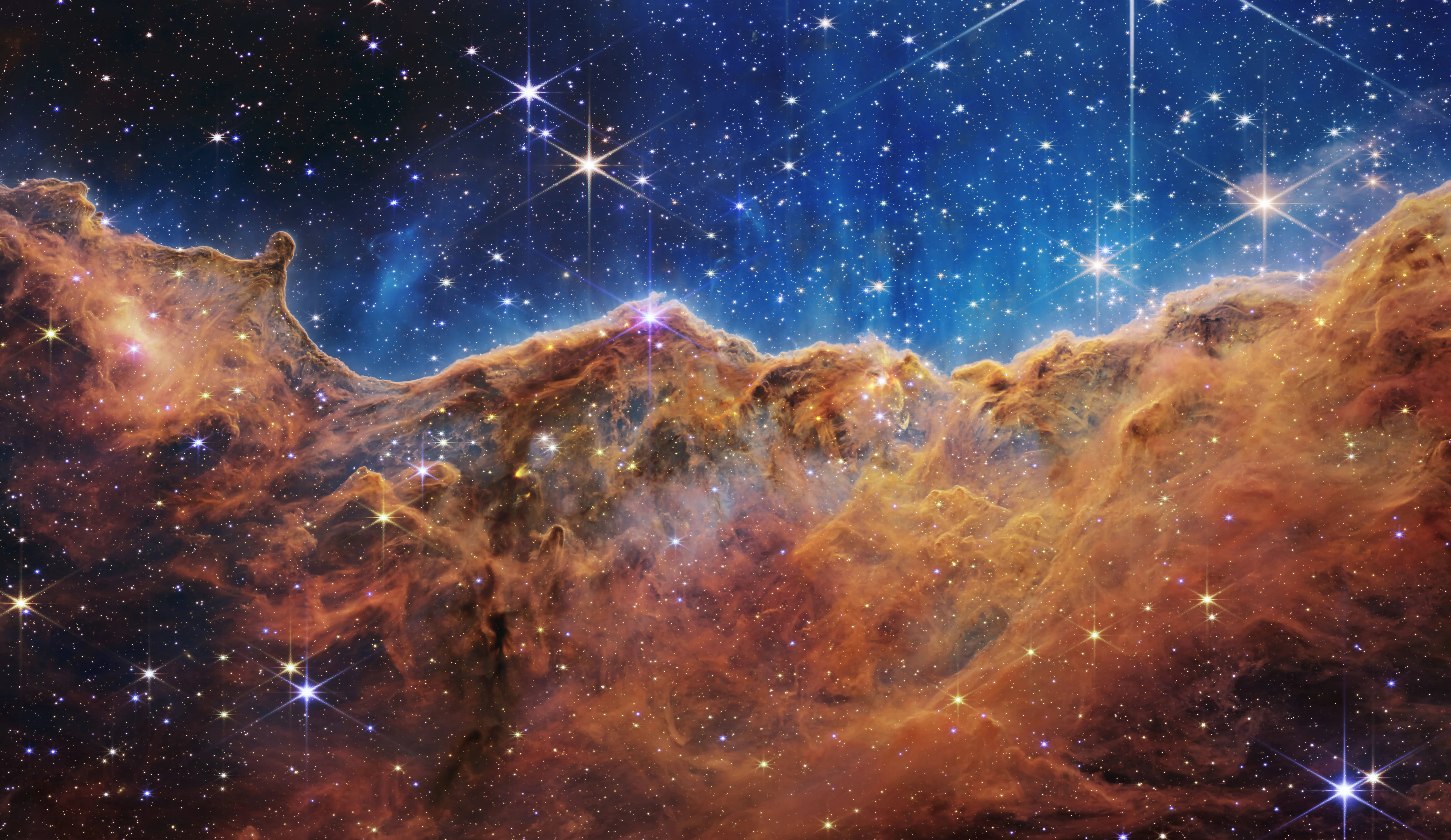 In this handout photo provided by NASA, a landscape of mountains and valleys speckled with glittering stars is actually the edge of a nearby, young, star-forming region called NGC 3324 in the Carina Nebula, on July 12, 2022 in space. Captured in infrared light by NASA's new James Webb Space Telescope, this image reveals for the first time previously invisible areas of star birth (Image via Getty)