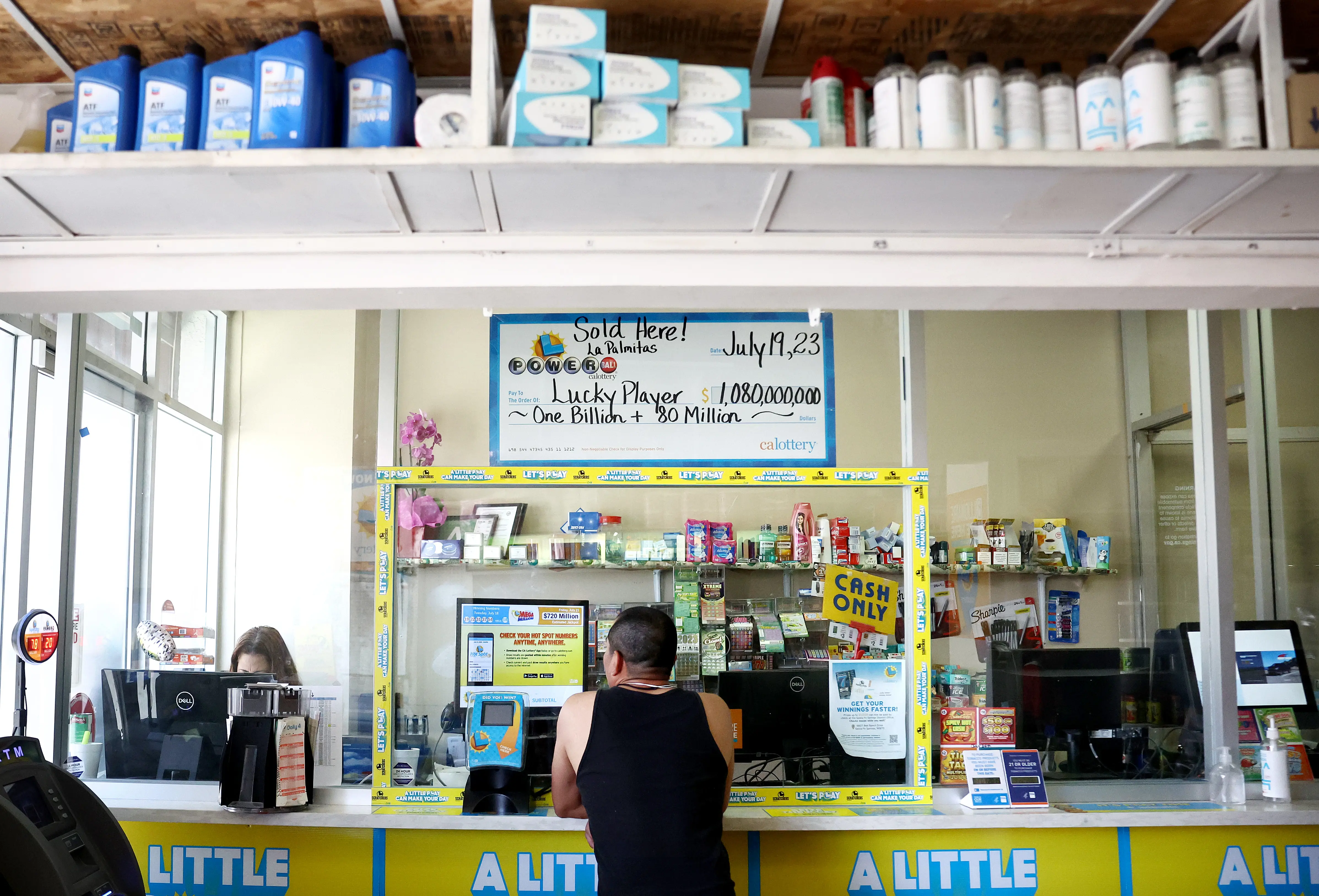 LOS ANGELES, CALIFORNIA - JULY 20: A customer stands beneath an enlarged symbolic check for $1.08 billion in Las Palmitas Mini Market on July 20, 2023 in Los Angeles, California. The $1.08 billion winning Powerball ticket was sold at the Las Palmitas Mini Market for the July 19th drawing. The jackpot is the third largest in Powerball history and was picked after three months of drawings without a winner. The mini market is located in the downtown Fashion District close to Skid Row. (Photo by Mario Tama/Getty Images)