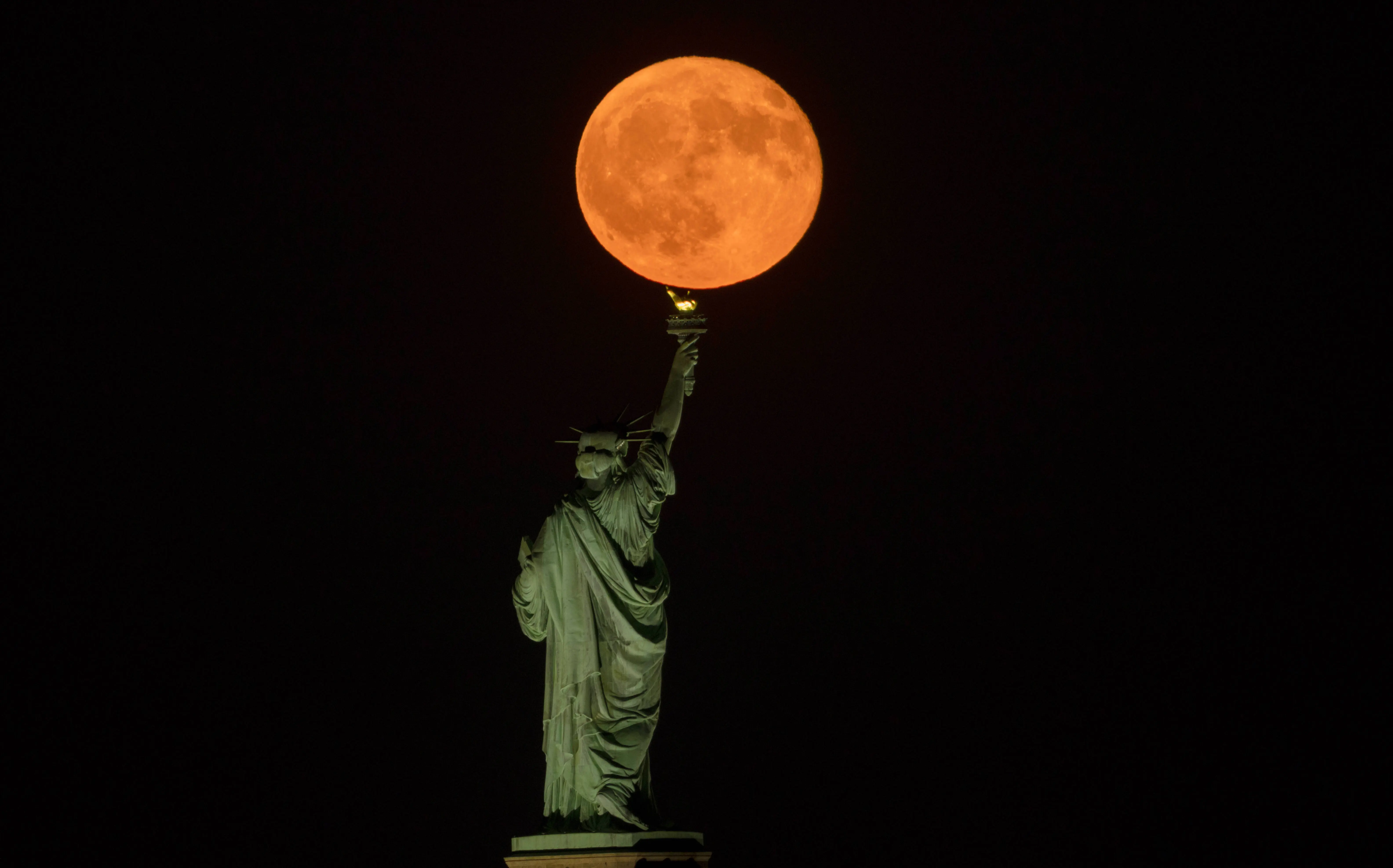 JERSEY CITY, NJ - AUGUST 9: The full Sturgeon Moon rises behind the Statue of Liberty in New York City on August 9, 2025, as seen from Jersey City, New Jersey (Image via Getty)