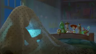 Toy Story 5 first-look art: Woody, Jessie, Buzz, Rex, Hamm, Bullseye, and Forky watch a tablet’s blue glow beneath a blanket fort. Photo: ©Disney/Pixar / Courtesy Pixar.com.