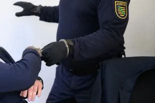 25 August 2025, Saxony, Chemnitz: A member of the judiciary removes the handcuffs from a defendant in the courtroom of the Chemnitz district court. The trial against the man and his wife for bribery and corruption involving millions of euros then begins. As the construction manager of a project company, the man is alleged to have paid bribes of almost five million euros to a joint company with his wife when awarding contracts to subcontractors. Photo: Hendrik Schmidt/dpa (Photo by Hendrik Schmidt/picture alliance via Getty Images)