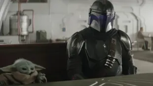 Din Djarin and Grogu sit at a cantina table, still from The Mandalorian and Grogu trailer. Image via from YouTube/@Star Wars