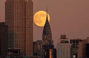 JERSEY CITY, NJ - NOVEMBER 15: The full Beaver Supermoon rises behind the Chrysler Building and the Empire State Building in New York City as the sun sets on November 15, 2024, as seen from Jersey City, New Jersey.  (Photo by Gary Hershorn/Getty Images)