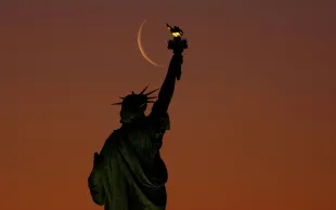 JERSEY CITY, NJ - MARCH 27: A five percent illuminated waning crescent moon rises behind the Statue of Liberty as the sun rises in New York City on March 27, 2025, as seen from Jersey City, New Jersey. (Photo by Gary Hershorn/Corbis News via Getty Images)