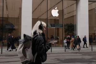 BERLIN, GERMANY - MARCH 25: A young woman, who said she did not mind being photographed, wears headphones and holds a smartphone as she walk past an Apple Store on March 25, 2024 in Berlin, Germany. The European Commission is launching an investigation into Apple, Meta (the parent company of Facebook) and Alphabet (the parent company of Google) over whether the companies violate the new EU Digital Markets Act. (Photo by Sean Gallup/Getty Images)