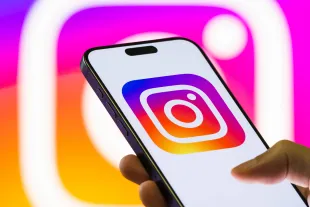 CHONGQING, CHINA - SEPTEMBER 4: In this photo illustration, a smartphone held in a hand shows the logo of Instagram, a popular social media and photo-sharing platform owned by Meta Platforms, with the company's branding seen in the background on September 4, 2025 in Chongqing, China. (Photo illustration by Cheng Xin/Getty Images)