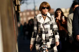 MILAN, ITALY - FEBRUARY 21: Anna Wintour wears sunglasses, a bejeweled necklace, a black and white checkered long trench coat, a floral print dress, outside Marni, during Milan Fashion Week Fall/Winter 2020-2021 on February 21, 2020 in Milan, Italy. (Photo by Edward Berthelot/Getty Images)