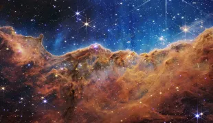 In this handout photo provided by NASA, a landscape of mountains and valleys speckled with glittering stars is actually the edge of a nearby, young, star-forming region called NGC 3324 in the Carina Nebula, on July 12, 2022 in space. Captured in infrared light by NASA's new James Webb Space Telescope, this image reveals for the first time previously invisible areas of star birth (Image via Getty)