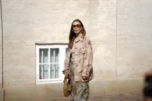 COPENHAGEN, DENMARK - AUGUST 5: Alana Hadid, attending the Skall Studio show during Copenhagen Fashion Week SS26, is seen wearing a beige and brown digital camouflage oversized button-up jacket with front flap pockets, long sleeves and small watermelon patches on the sleeves; a taupe crew-neck T-shirt underneath; wide-leg drawstring field cargo trousers in a earth tone colored camouflage design from Henrik Vibskov; a khaki nylon pouch-style handbag with a knotted top handle; square-shaped tortoiseshell sunglasses with rounded glasses; large gold and silver abstract-shaped hoop earrings; her straight brown hair is worn loose with a center part during Copenhagen Fashion Week day two on August 5, 2025 in Copenhagen, Denmark.  (Photo by Moritz Scholz/Getty Images)