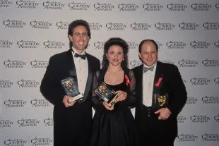 American comedian and actor Jerry Seinfeld, wearing a tuxedo and bow tie, American actress and comedian Julia Louis-Dreyfus, who wears a black evening gown with sheer black sleeves, and American actor and comedian Jason Alexander, also in a tuxedo and bow tie, in the 7th Annual American Comedy Awards press room, at the Shrine Exposition Center in Los Angeles, California, 28th February 1993. Seinfeld holds his 'Funniest Male Performer in a TV Series (Network, Cable or Syndication),' Louis-Dreyfuss has her 'Funniest Supporting Female Performer in a TV Series' award, and Alexander his 'Funniest Supporting Male Performer in a TV Series' award, all received for their NBC sitcom 'Seinfeld'. (Photo by Vinnie Zuffante/Getty Images)