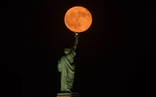 JERSEY CITY, NJ - AUGUST 9: The full Sturgeon Moon rises behind the Statue of Liberty in New York City on August 9, 2025, as seen from Jersey City, New Jersey (Image via Getty)